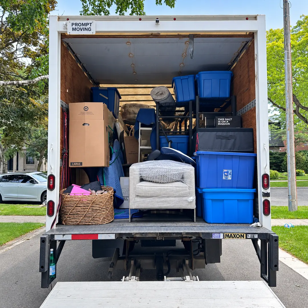 Household furniture, wrapped chair and blue storage bins inside Prompt Moving’s truck